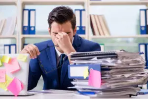 Hombre adulto en oficina con signos de estrés y sobrecarga de trabajo, ilustrando el impacto del TDAH en la organización y concentración